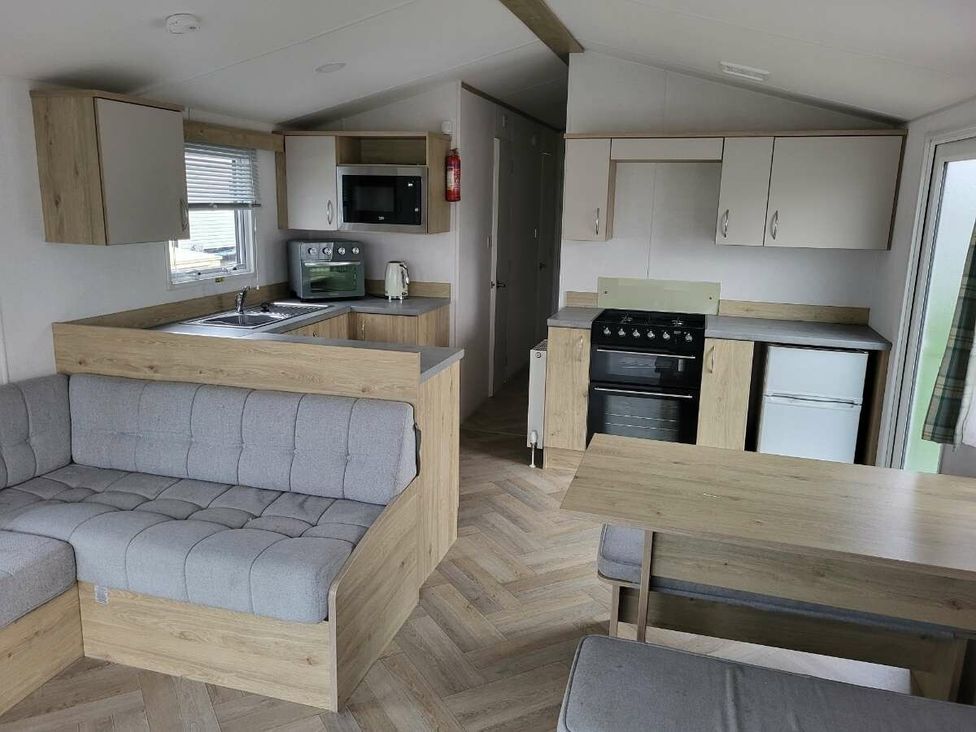 a kitchen and living area with a gray sofa and wooden furniture at Ty Mawr Holiday Park - Holiday Accommodation 21121 Ty Mawr