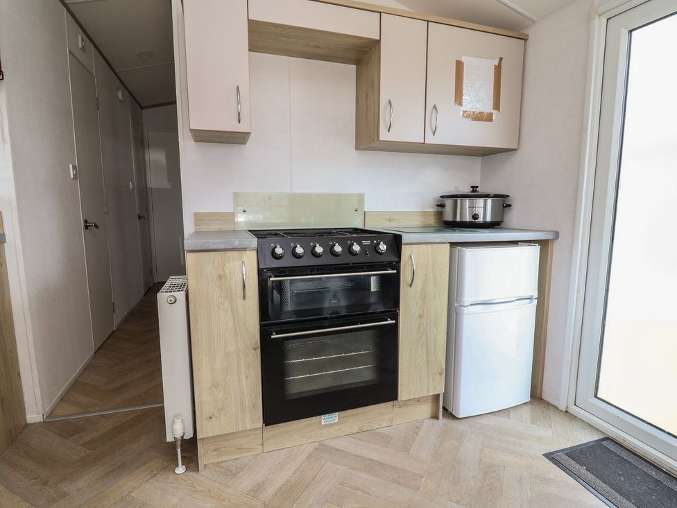 A kitchen with an oven, cupboards, fridge, and slow cooker at Ty Mawr Holiday Park - Ty Mawr