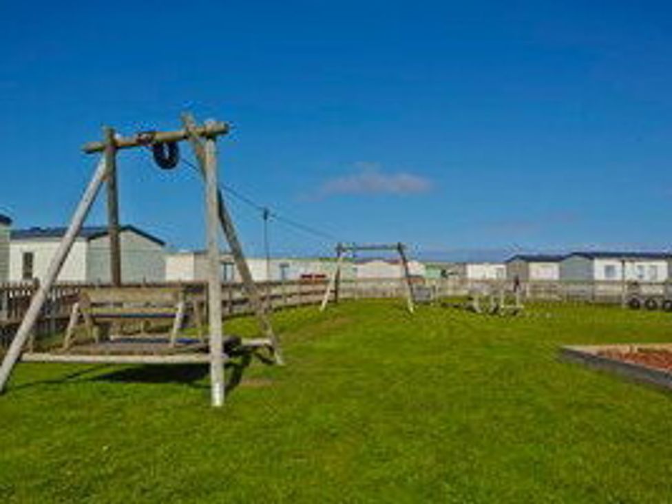 a playground area with swings and grass at Whitehouse Leisure Park - Holiday Accommodation 21355, Towyn