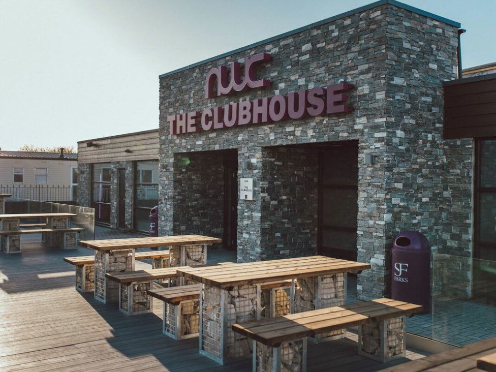 an exterior view of a building with stone walls and wooden benches at Whitehouse Leisure Park - Holiday Accommodation 21355 in Towyn