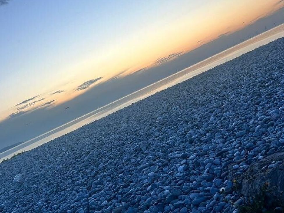 a pebble beach with a sunset over the water at Whitehouse Leisure Park - Holiday Accommodation 21355 in Towyn