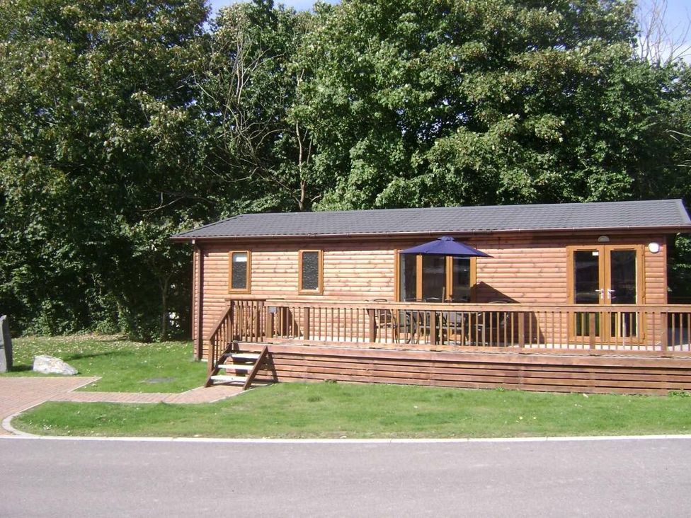 a wooden holiday lodge with a deck and outdoor seating at St Minver Holiday Park - Holiday Accommodation 21443 Wadebridge