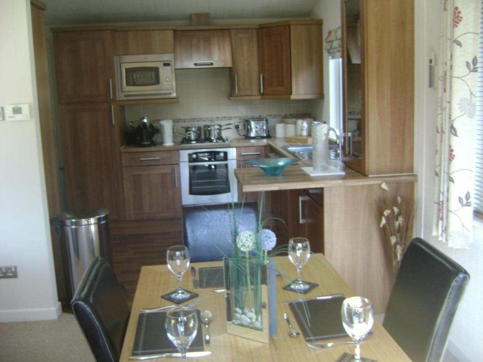 a kitchen with wooden cabinets and dining table set at St Minver Holiday Park - Holiday Accommodation 21443 Wadebridge
