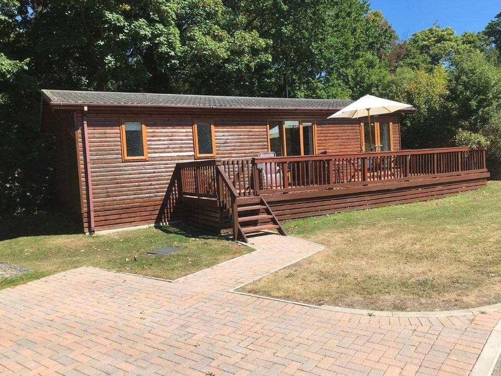 a wooden cabin with a deck and an umbrella surrounded by grass at St Minver Holiday Park - Holiday Accommodation 21443 in Wadebridge