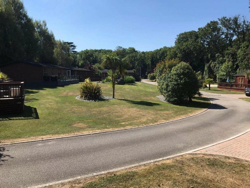 a paved road winding through a landscaped area with holiday cabins and trees at St Minver Holiday Park - Holiday Accommodation 21443 in Wadebridge