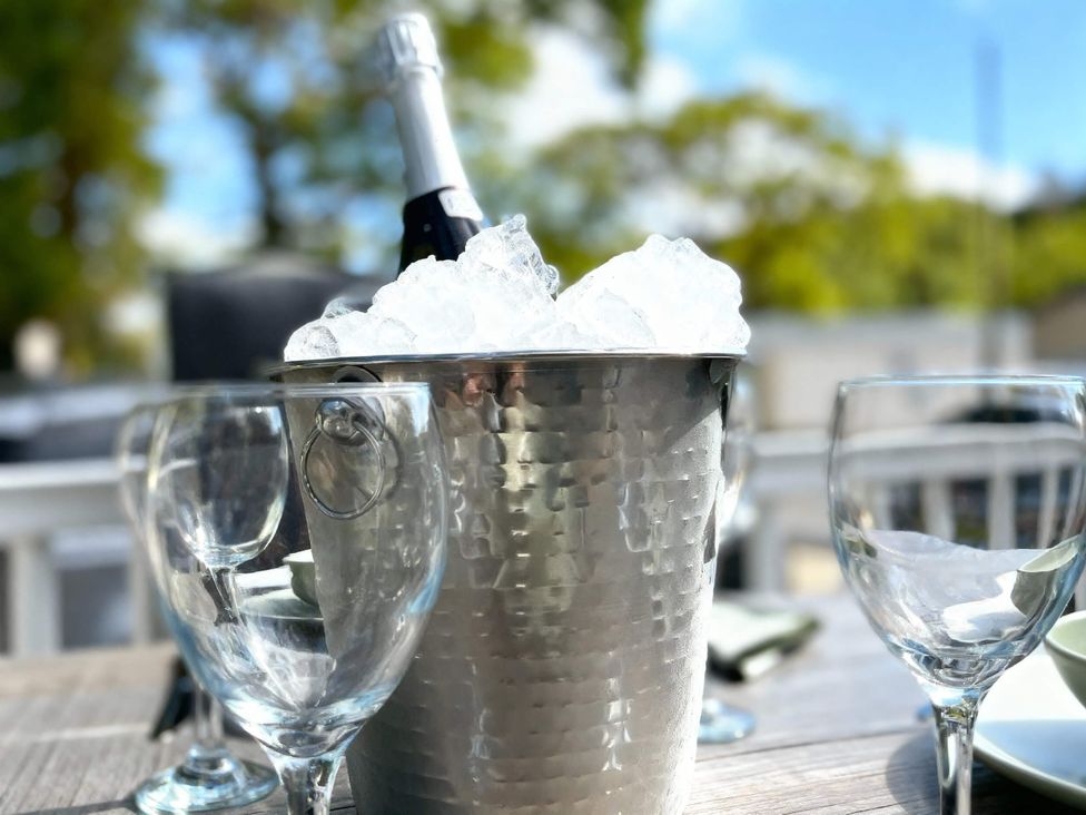 An ice bucket with champagne and wine glasses in an outdoor dining area at Aberdunant Hall Holiday Park - Holiday Accommodation 21962, Prenteg