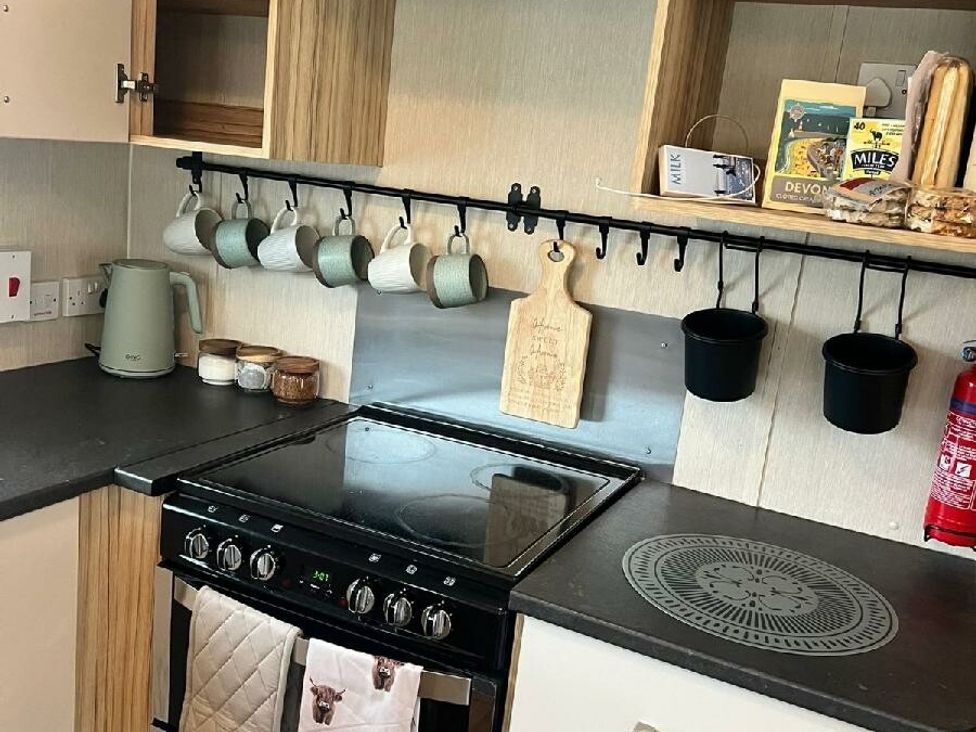 a kitchen with a stove, hanging mugs, and various kitchen items at Hoburne Devon Bay - Holiday Accommodation 22090 in Paignton