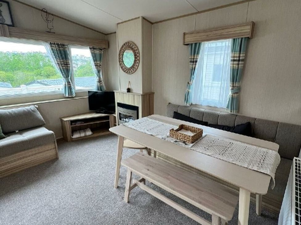 a living room with a TV, seating area, dining table, and windows at Hoburne Devon Bay - Holiday Accommodation 22090 in Paignton