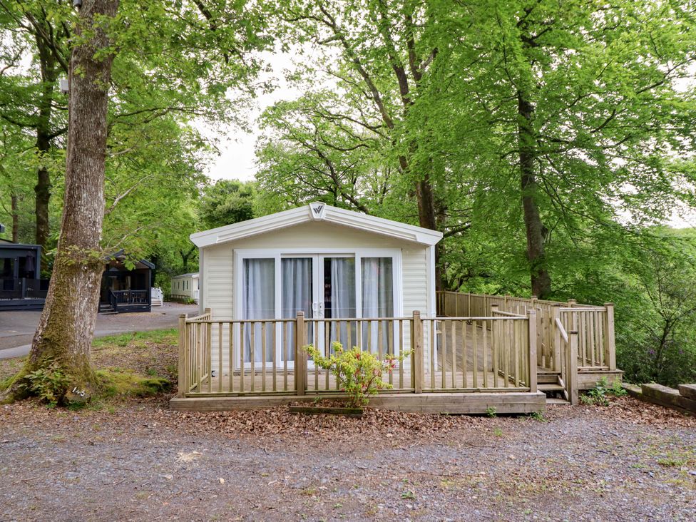 A cabin with decking surrounded by trees at 145 Woodside View in Porthmadog