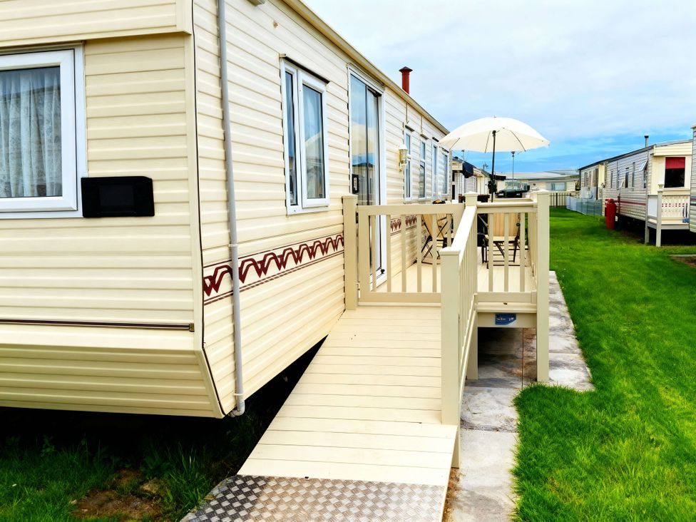 A caravan with a decking and umbrella at Coastfield Holiday Village - Holiday Accommodation 2604 in Ingoldmells