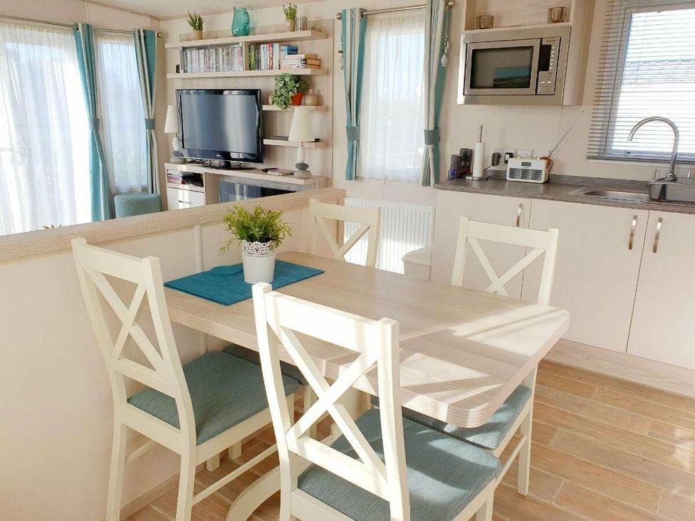 a dining area with a table and four chairs in a room with a kitchen and living space at Shorefield Country Park - Holiday Accommodation 3042 in Milford On Sea