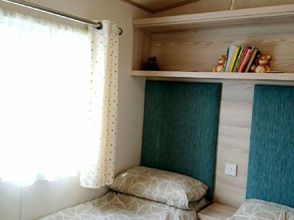 a bedroom with twin beds and a shelf containing books and toys at Shorefield Country Park - Holiday Accommodation 3042, Milford On Sea