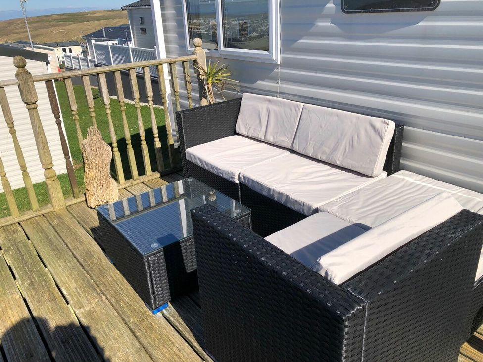a seating area with black wicker furniture and a glass table at Liskey Hill Caravan Park - Holiday Accommodation 3043 Perranporth