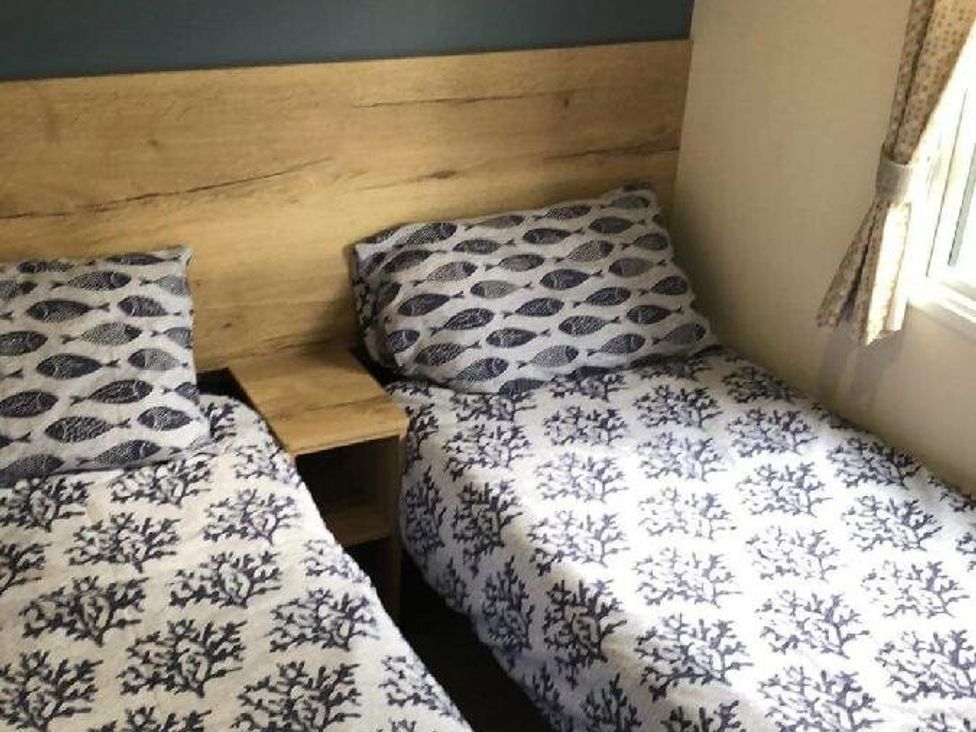 a bedroom with two beds and a wooden headboard at Liskey Hill Caravan Park - Holiday Accommodation 3043 in Perranporth