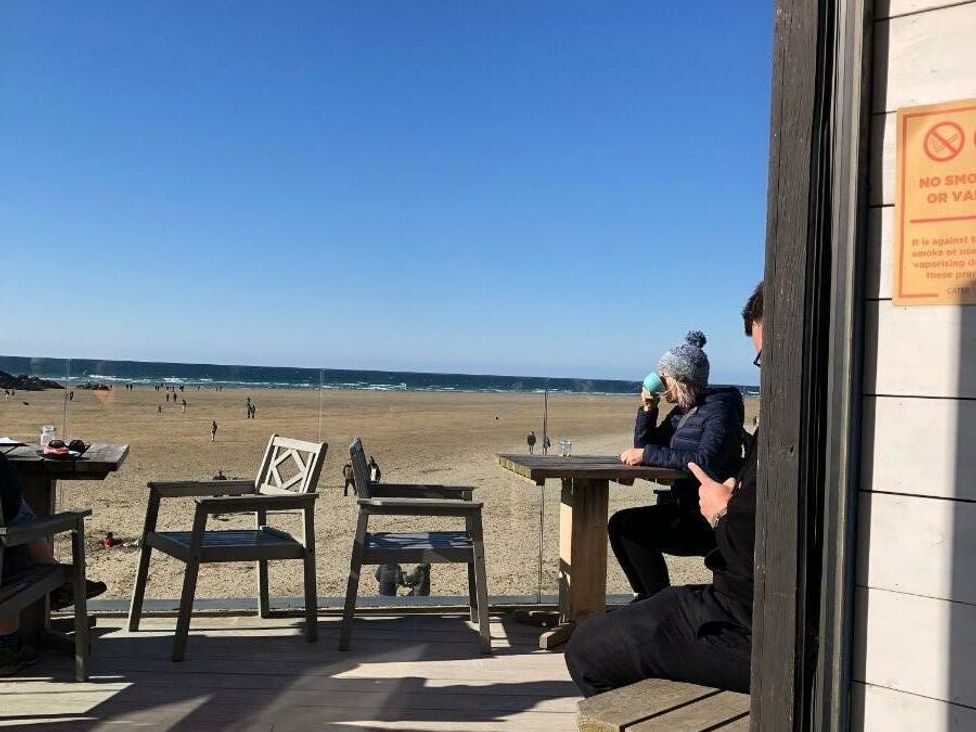 a beach view from a deck with people in the distance at Liskey Hill Caravan Park - Holiday Accommodation 3043, Perranporth