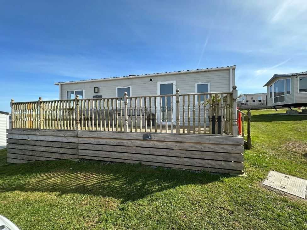 a mobile home with a wooden deck on a grassy area at Liskey Hill Caravan Park - Holiday Accommodation 3043, Perranporth