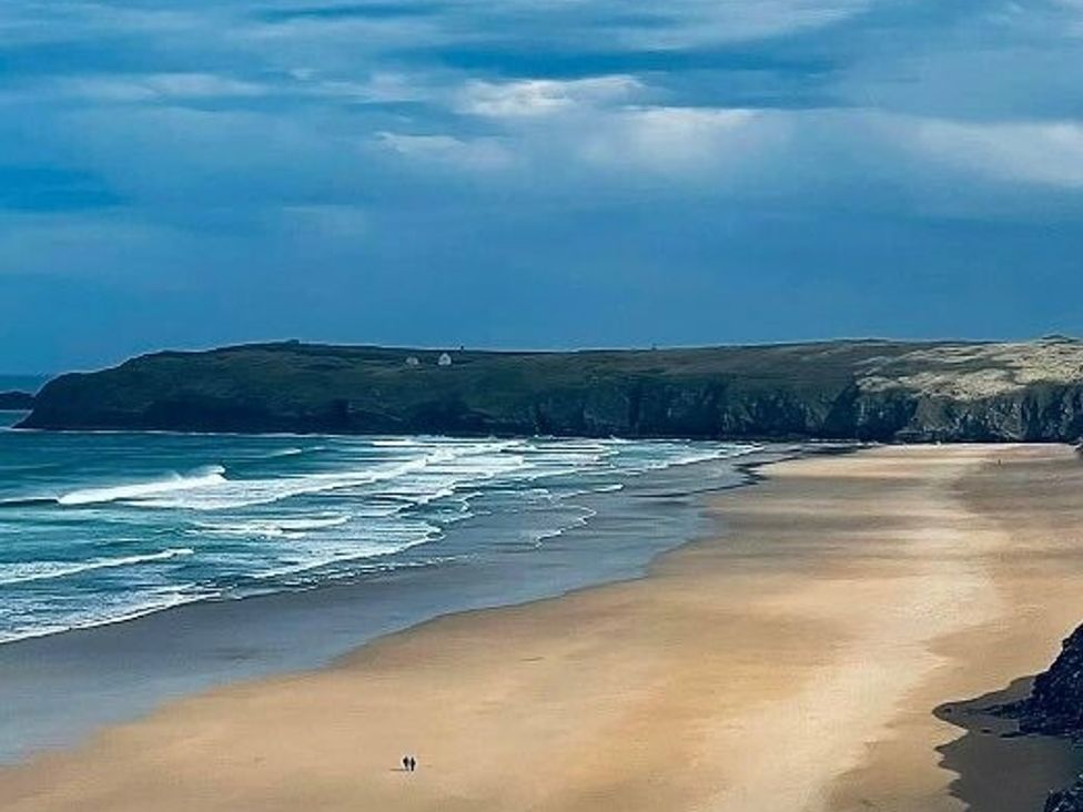 a beach with waves and cliffs in the background at Liskey Hill Caravan Park - Holiday Accommodation 3043, Perranporth