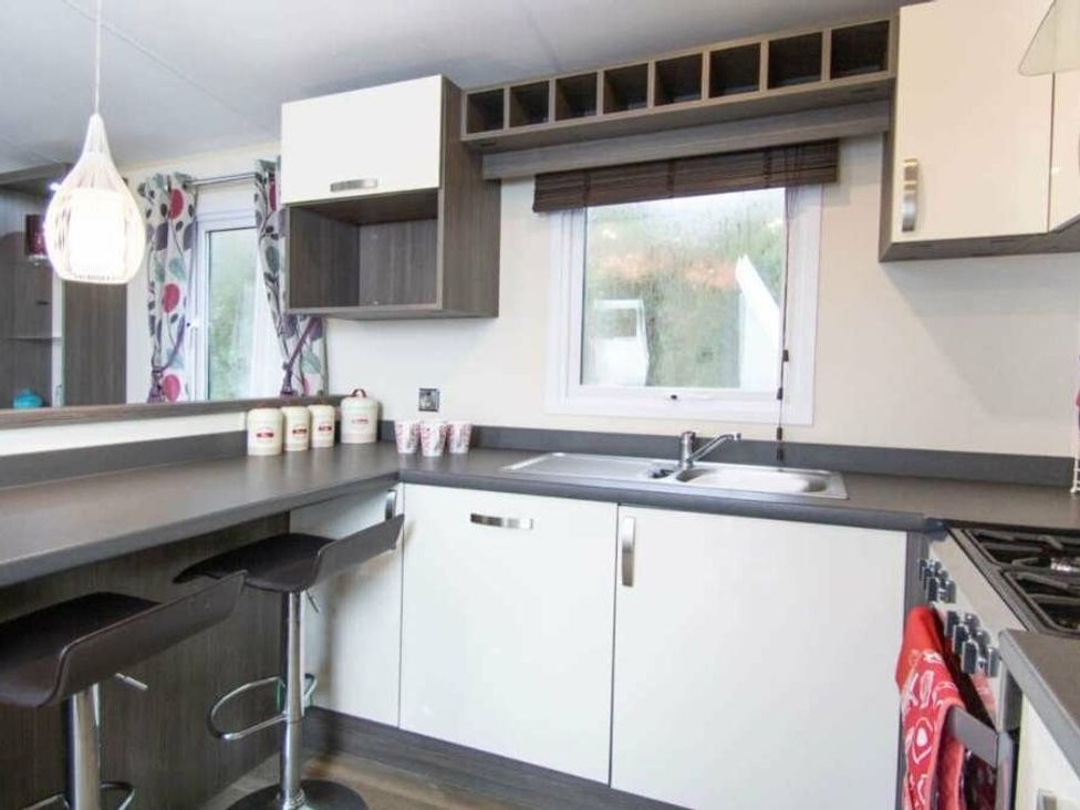 a small kitchen with a sink and bar stools at Shorefield Country Park - Holiday Accommodation 4132, Milford On Sea