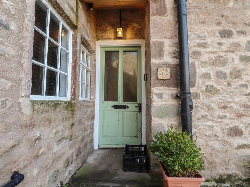 An entrance with a green front door and stone wall at The Snug in Morecambe
