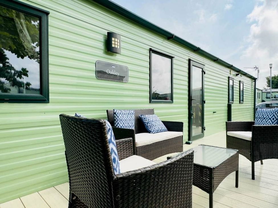 a seating area with wicker furniture and a glass table outside a green building at St Andrews Holiday Park - Holiday Accommodation 609 in St. Andrews