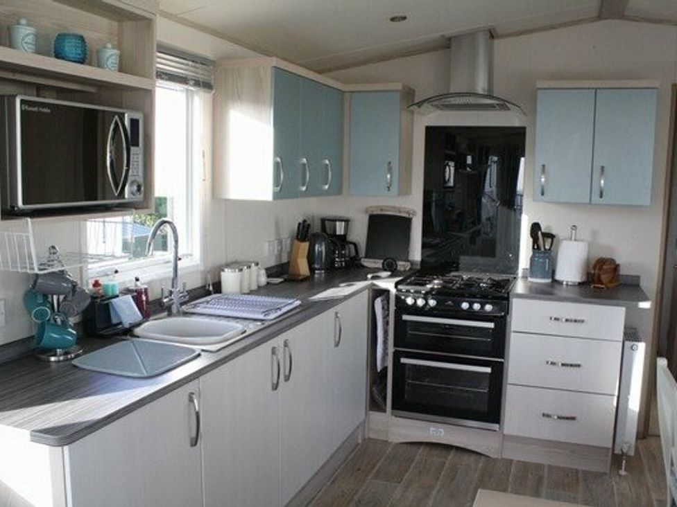 a modern kitchen with gray and blue cabinets, sink, stove, and various appliances at Durdle Door Holiday Park - Holiday Accommodation 6617 in Wareham