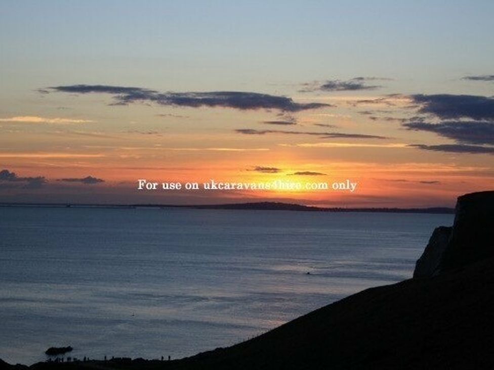 a sunset over the ocean with cliffs in the foreground at Durdle Door Holiday Park - Holiday Accommodation 6617, Wareham