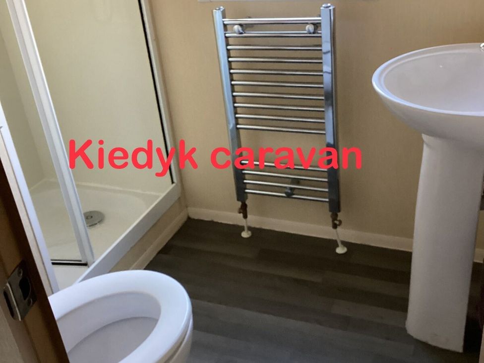 a bathroom with a shower, towel radiator, sink, and toilet at Kiedyk caravan in Skegness