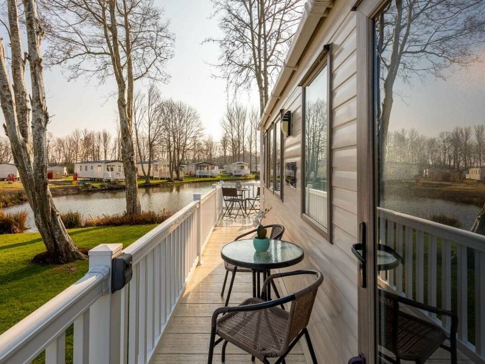 a deck with a table and chairs beside a pond at Haggerston Castle - Holiday Accommodation 779 in Berwick-upon-Tweed