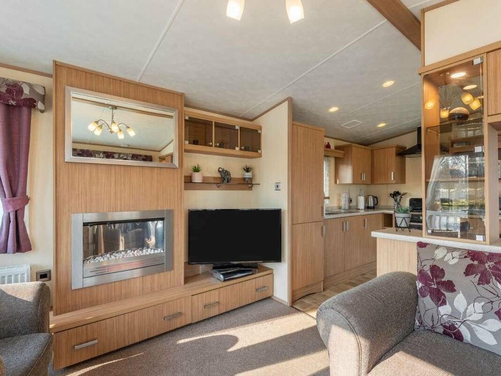 a living room with a wall-mounted television, fireplace, and kitchen area at Haggerston Castle - Holiday Accommodation 779 in Berwick-upon-Tweed