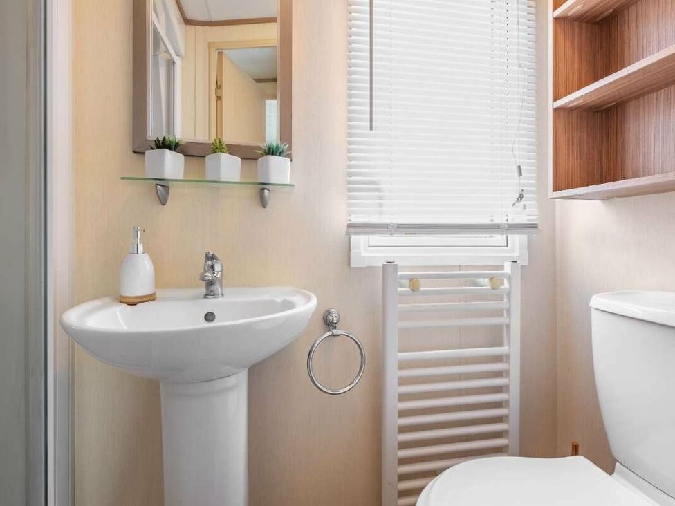 a bathroom featuring a sink, toilet, towel radiator, and shelves at Haggerston Castle - Holiday Accommodation 779 in Berwick-upon-Tweed