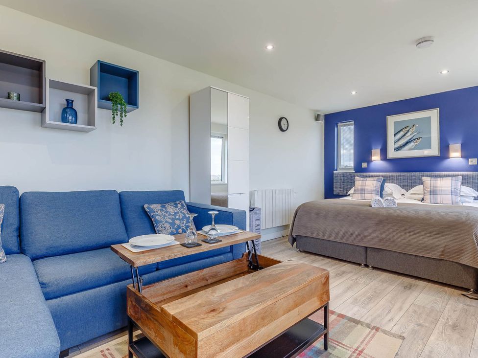 A studio room featuring a sofa, table, and bed at Lakeside Studio in Portreath