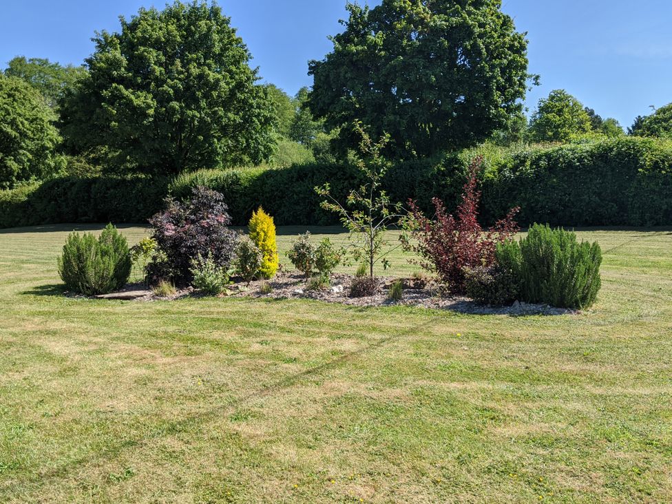 A garden with a flower bed surrounded by grass at The Bullpen in West Tytherley