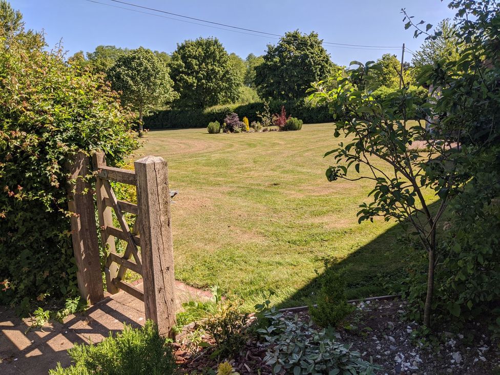 A garden with a gate leading to a grassy area and trees at The Bullpen@Manor Farm West Tytherley