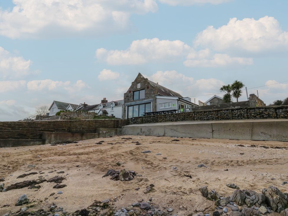 A beach with a house and palm trees at The Boat House - Port Eynon