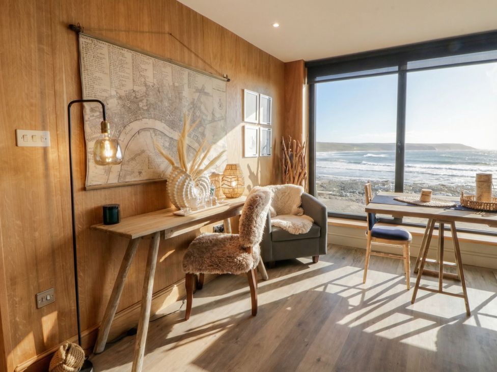 A living room with a table and chair near a window at The Boat House - Port Eynon