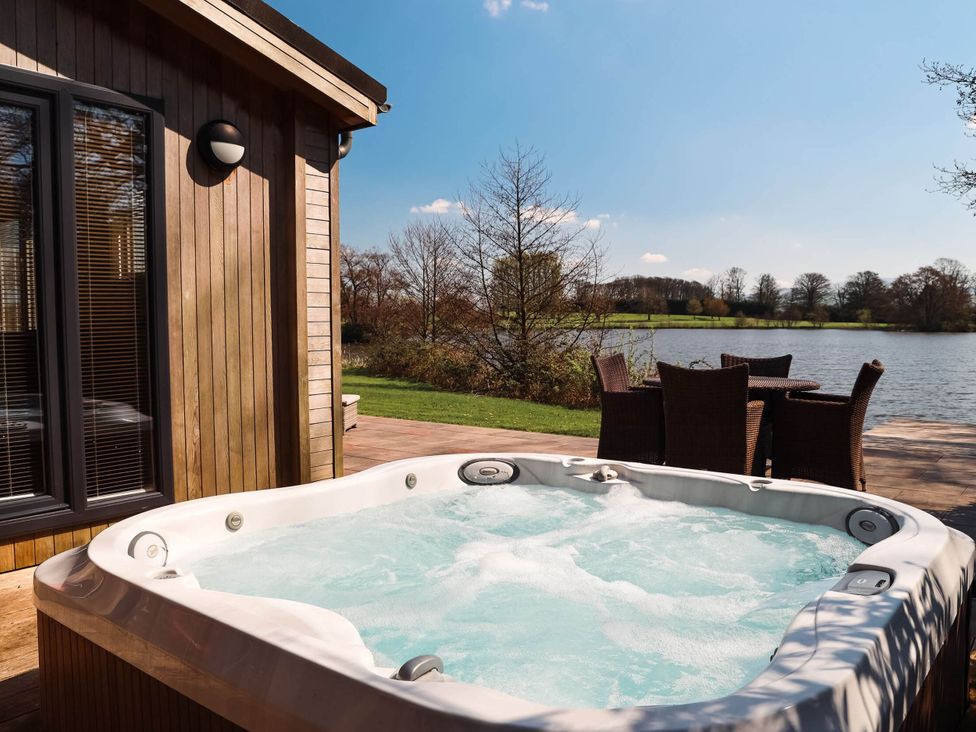 An outdoor area with a hot tub and seating near a lake at Lawson in Wigton