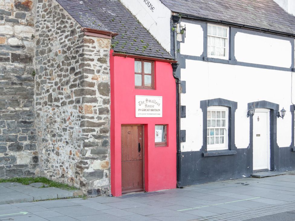 A red house with a sign next to a stone wall at The Smallest House in Conwy