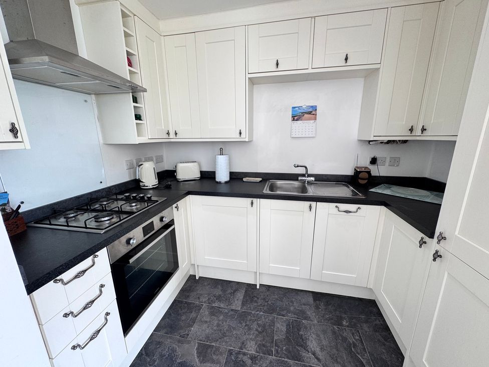 A kitchen with cabinets, stove, sink, and kettle at Ty Nain in Bodorgan