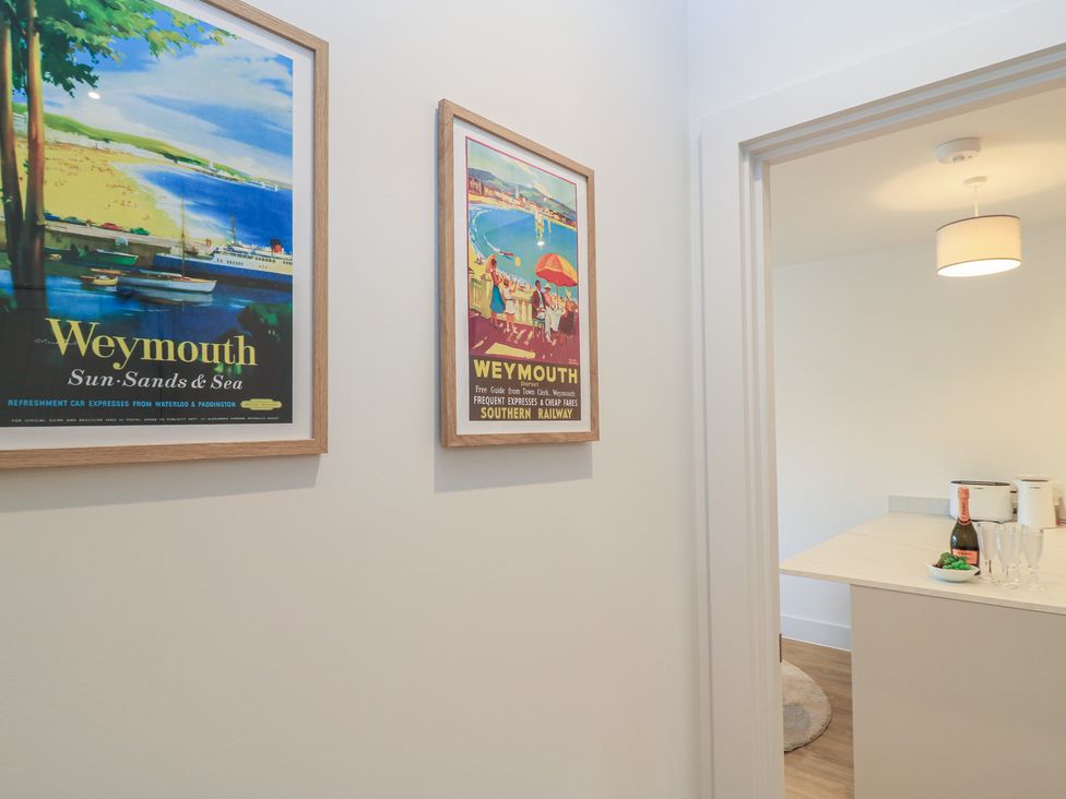 A hallway with framed posters and a view of a kitchen counter at Brewery View in Weymouth