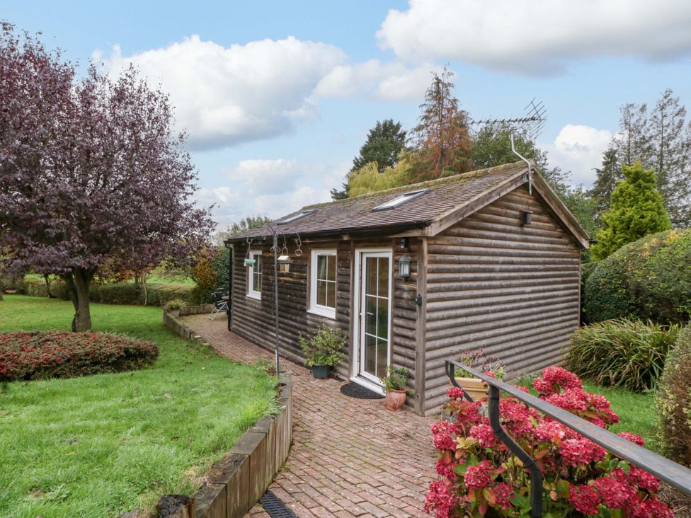 A wooden cabin in a garden with a pathway and flowers at The Log Cabin in Corse near Gloucester
