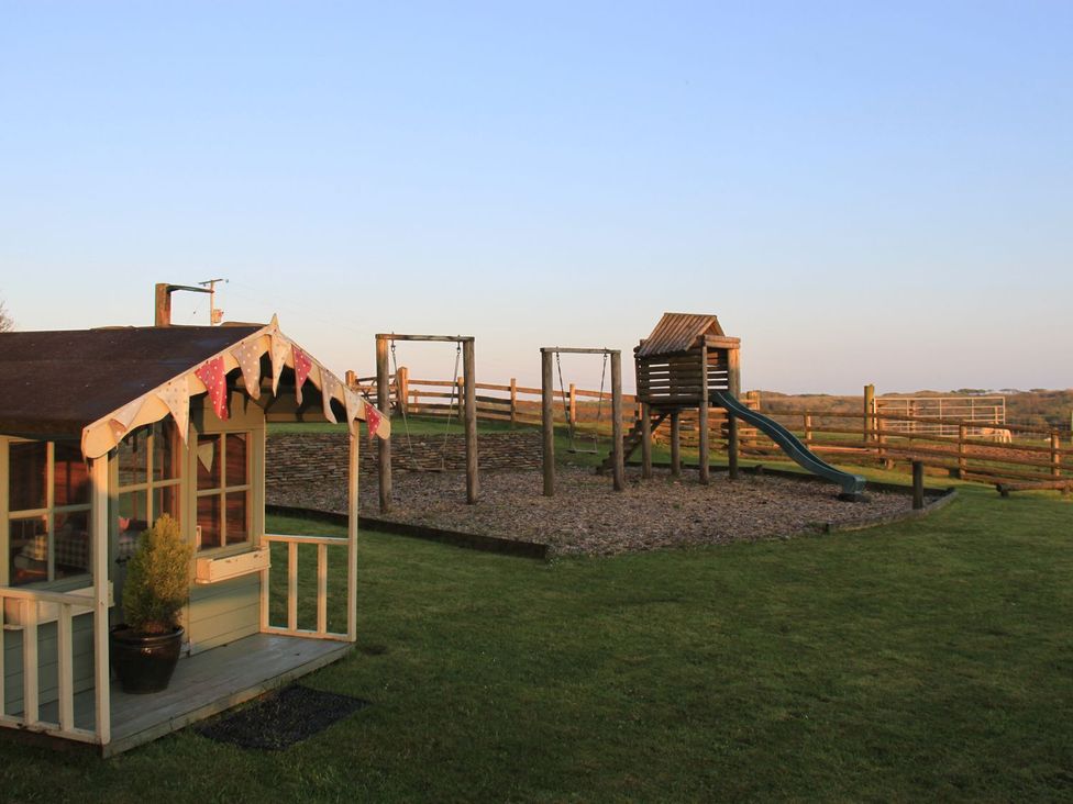 An outdoor area with a playhouse and playground equipment at Higher Forda in Holsworthy