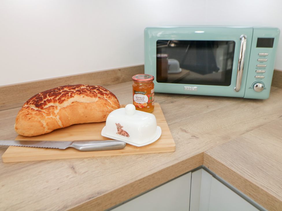 A kitchen countertop with bread, butter dish, knife, jar of marmalade, and a microwave at Shunter’s Nook in Colwich