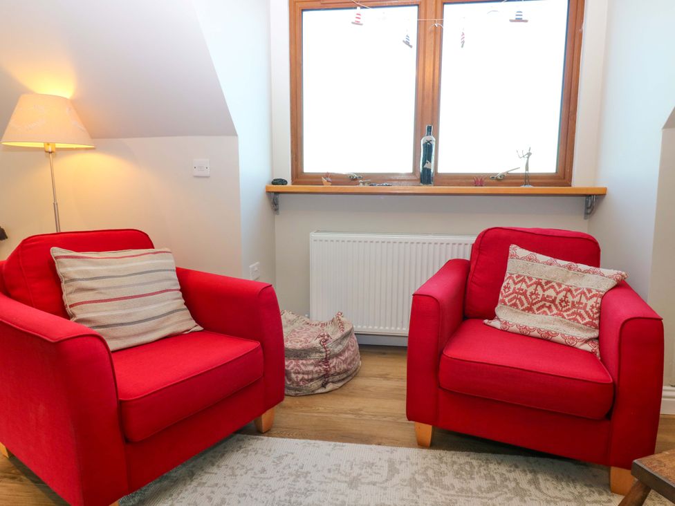A living room with red armchairs and a lamp at Bridle Cottage in Cove