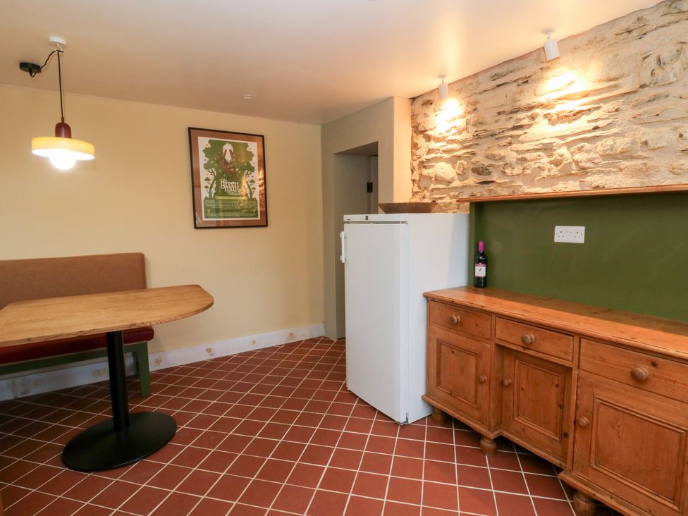 A kitchen with a table, bench, fridge, and cabinet at Fronglyd Aberporth