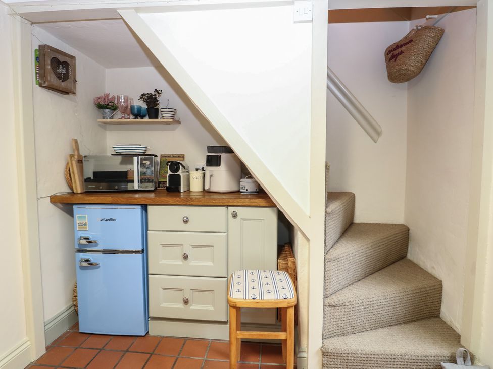 A small kitchen area with appliances and a staircase at Beeble Cottage in Fakenham