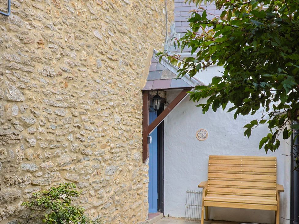 An outdoor area with a stone wall and a wooden bench at Vine Cottage in Burton Bradstock