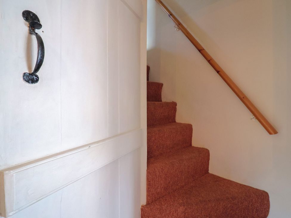 A staircase with a handrail and door at Vine Cottage in Burton Bradstock