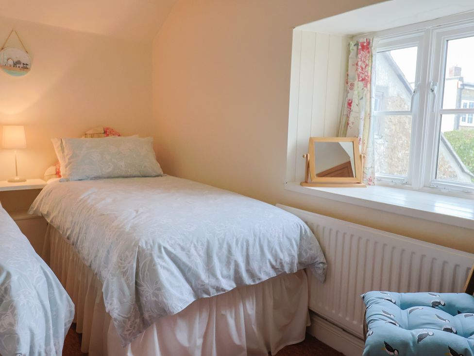 A bedroom with two beds, a lamp, and a window at Vine Cottage in Burton Bradstock