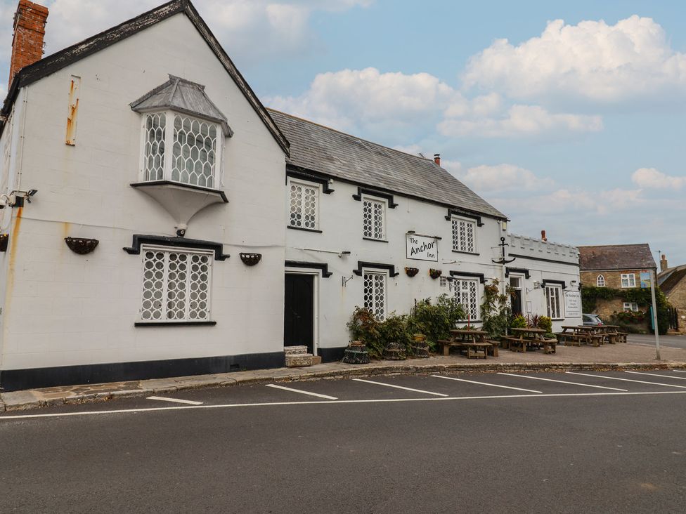 A pub with a sign and outdoor seating at The Anchor Inn in Burton Bradstock