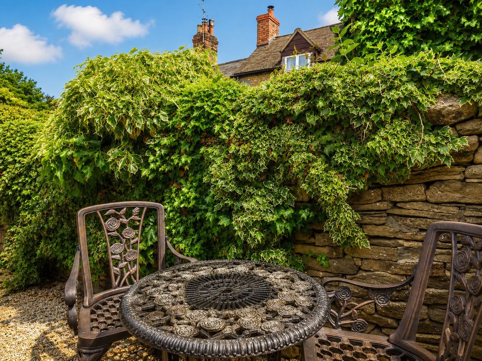 A garden with a stone wall and metal table and chairs at 29 Spring Street in Chipping Norton